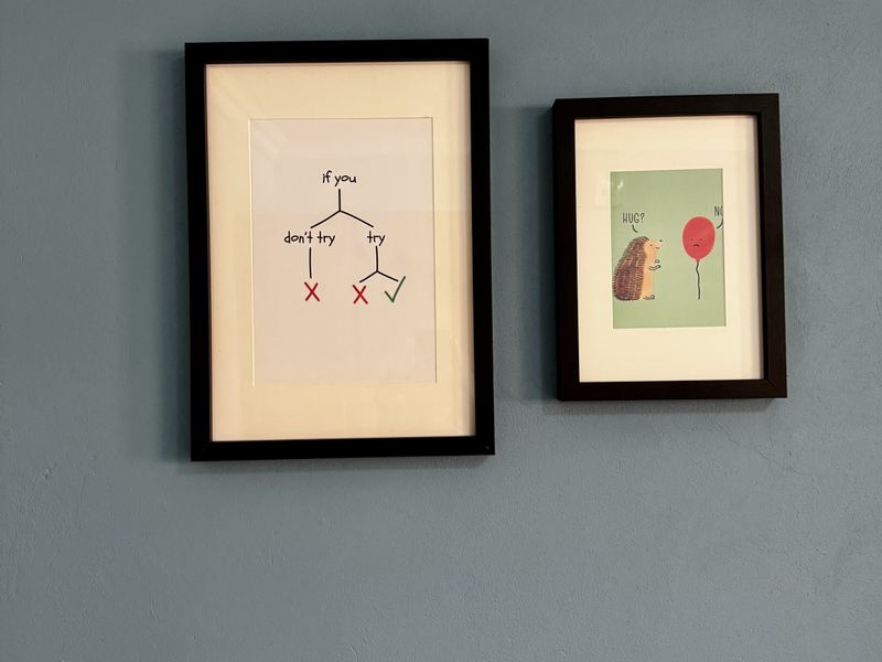 A close-up view of two framed prints hanging on a blue painted wall.