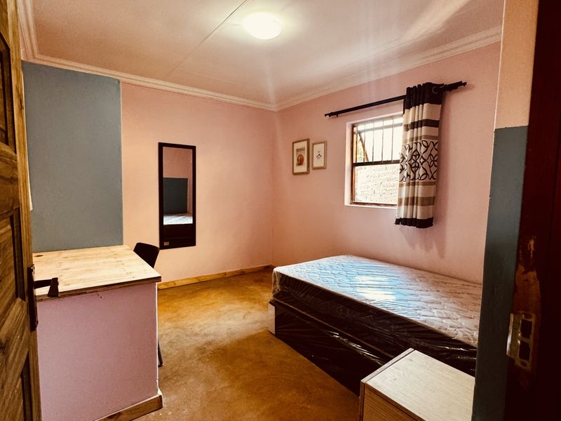 A bedroom featuring pink and blue painted walls, a window with security bars, and a simple floor finish.