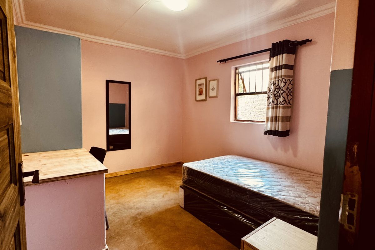 A bedroom featuring pink and blue painted walls, a window with security bars, and a simple floor finish.