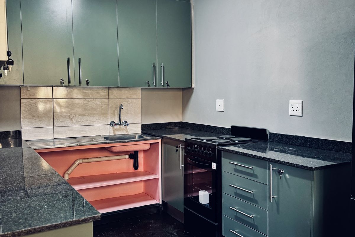 A functional kitchen featuring green cabinetry, granite countertops, and a tiled backsplash, currently requiring repairs to the under-sink cabinetry and flooring.
