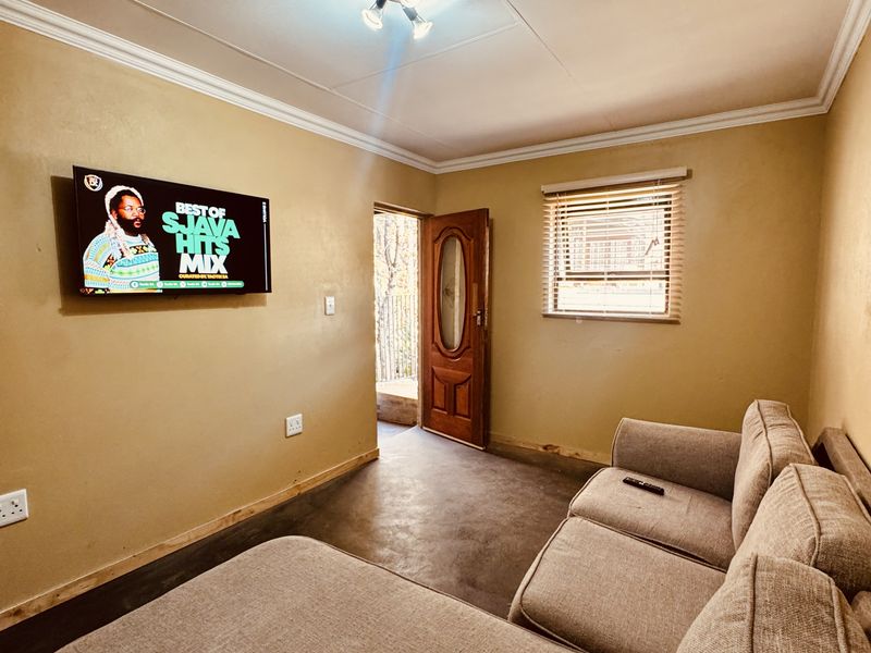 A compact living room featuring neutral walls, tiled flooring, a ceiling light fixture, and direct access to an outdoor area.