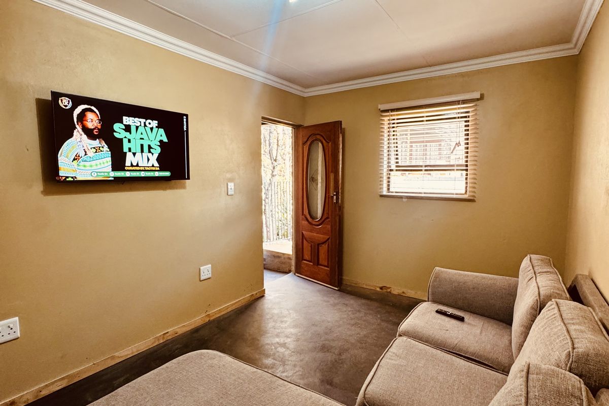 A compact living room featuring neutral walls, tiled flooring, a ceiling light fixture, and direct access to an outdoor area.