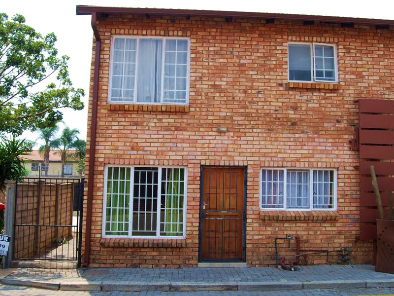 Front elevation of a double-storey townhouse featuring face brick construction, secure entrance gate, and paved exterior area.