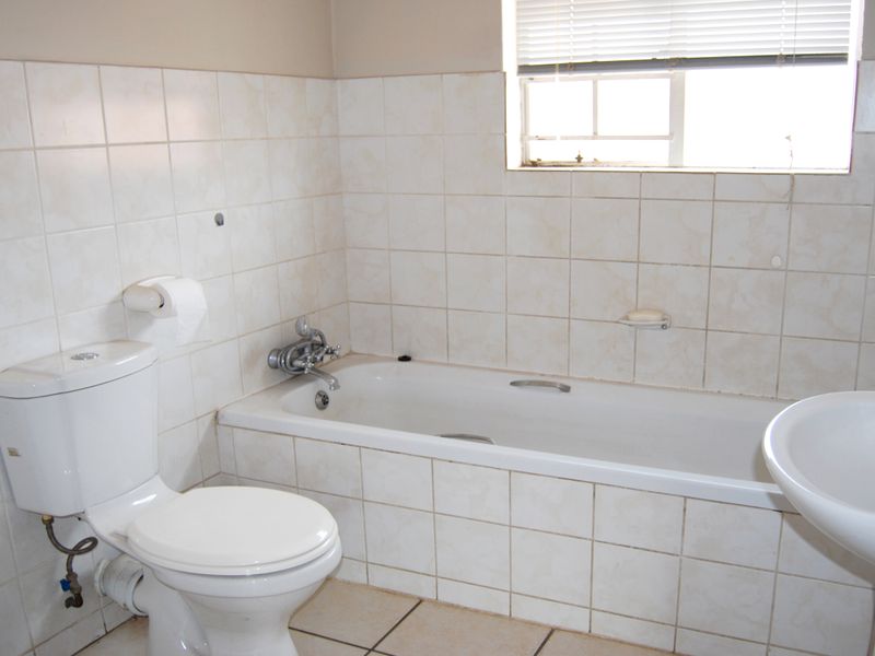 A dated bathroom featuring a standard bathtub, pedestal basin, and toilet with neutral ceramic wall and floor tiling.