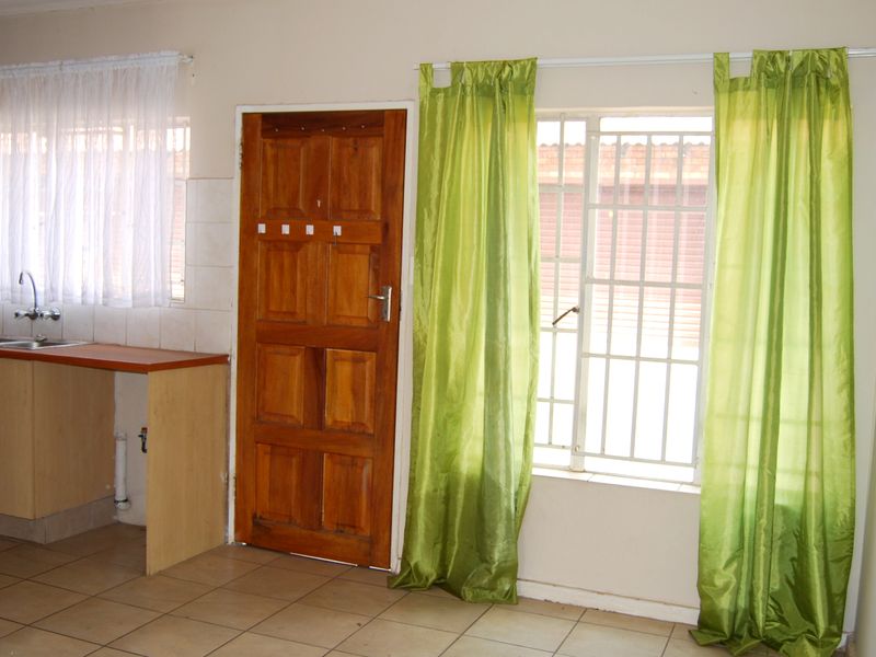 A functional kitchen area featuring laminate cabinetry, a stainless steel sink, and tiled flooring, with direct access to the exterior via a wooden door.
