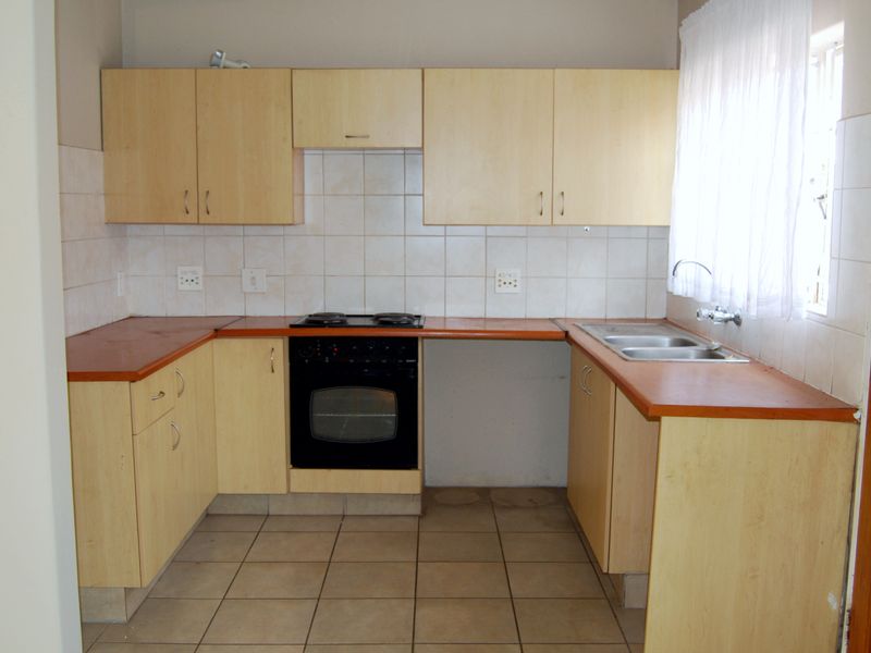 A functional kitchen featuring light wood-tone cabinetry, laminate countertops, a built-in oven with hob, and tiled flooring, offering a clean and practical workspace.