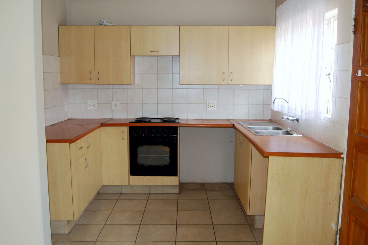 A functional kitchen featuring light wood-tone cabinetry, laminate countertops, a built-in oven with hob, and tiled flooring, offering a clean and practical workspace.