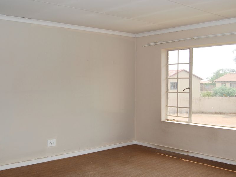 An empty bedroom featuring carpeted flooring, coved ceilings, and a large window with security bars overlooking the exterior grounds.