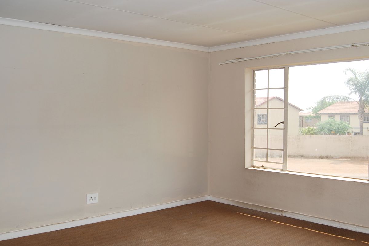 An empty bedroom featuring carpeted flooring, coved ceilings, and a large window with security bars overlooking the exterior grounds.