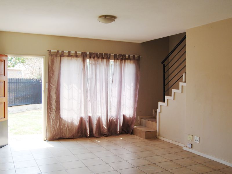 An open-plan living area featuring tiled flooring, a staircase with a metal balustrade, and direct access to the outdoor space.