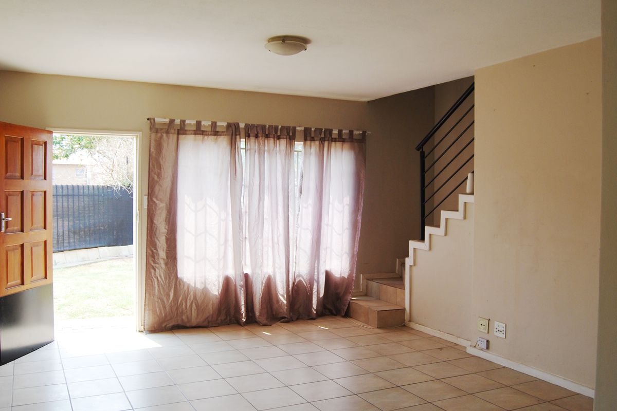 An open-plan living area featuring tiled flooring, a staircase with a metal balustrade, and direct access to the outdoor space.