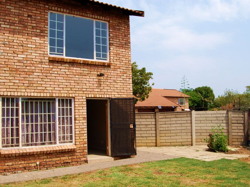 Rear view of a double-storey face brick townhouse featuring a paved patio area, security gates, and a private garden enclosed by a precast boundary wall.
