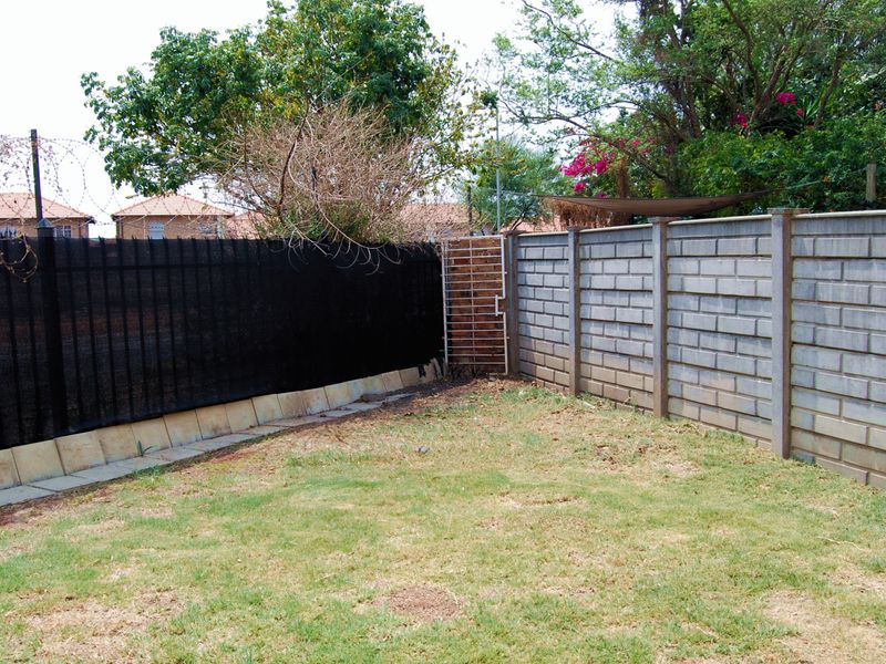 A private backyard area featuring a grass lawn enclosed by a combination of concrete block walls and metal security fencing with razor wire.