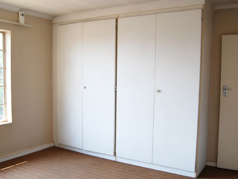 A vacant bedroom featuring built-in cupboards, a window with security bars, and carpeted flooring, ready for a modern update.