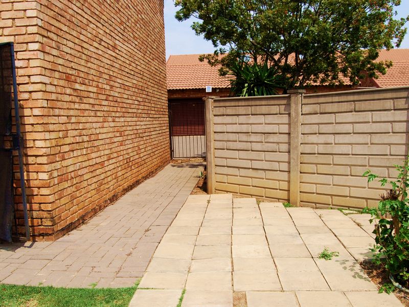 A side exterior view of the townhouse featuring a brick facade, paved walkway, and a precast concrete boundary wall.