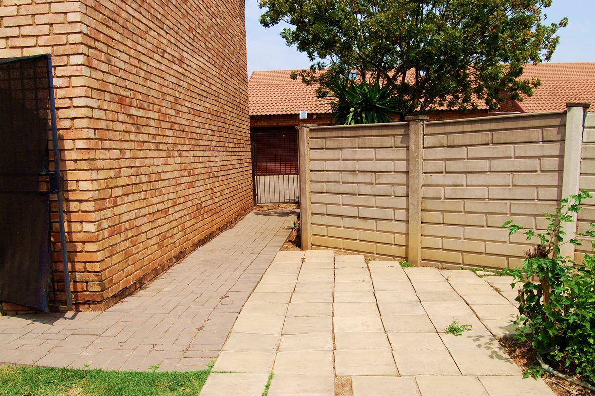 A side exterior view of the townhouse featuring a brick facade, paved walkway, and a precast concrete boundary wall.
