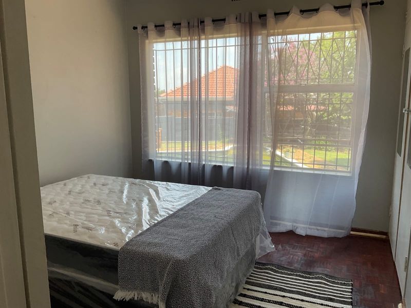 A bedroom featuring parquet flooring, a large window with security bars, and a built-in cupboard.
