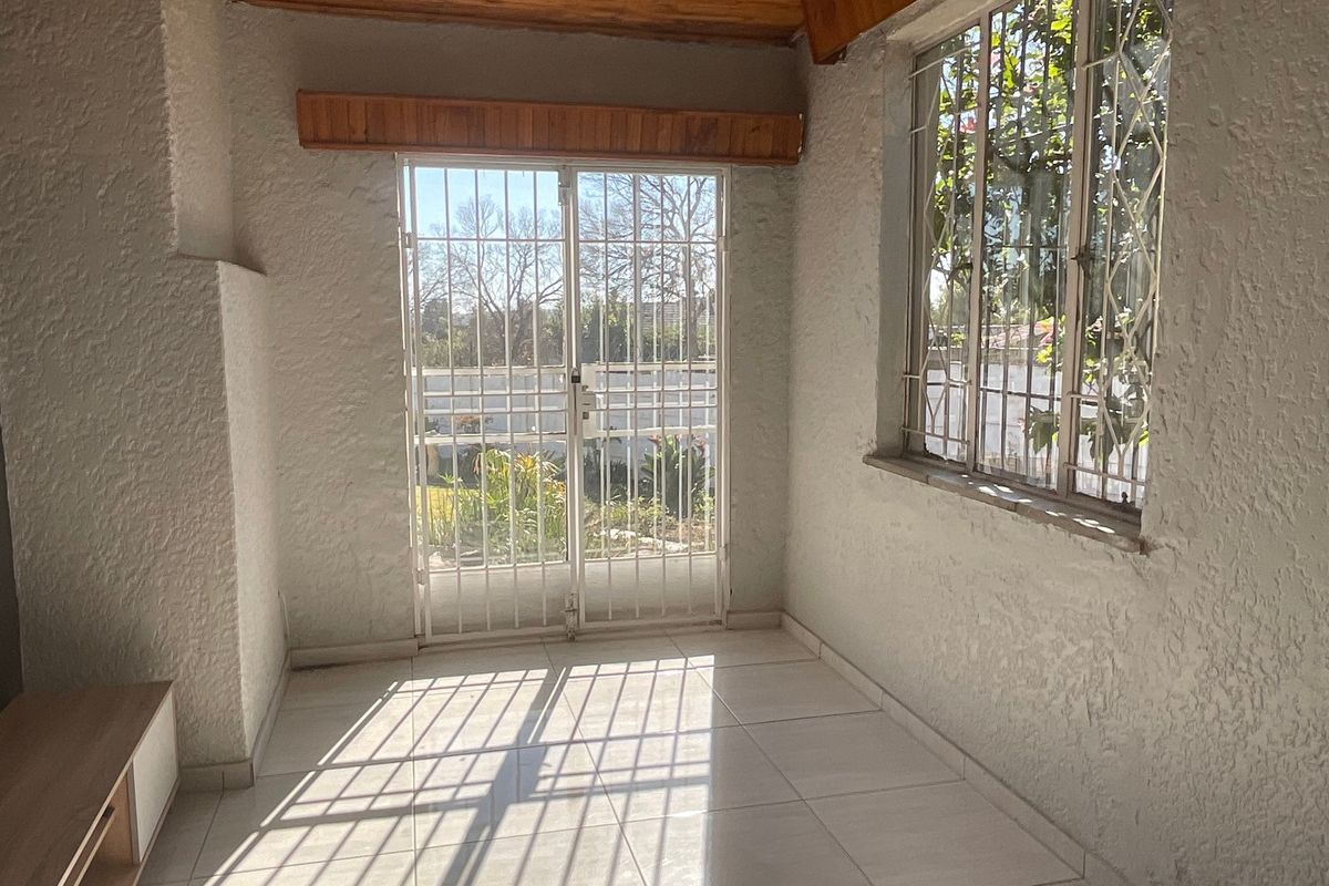 An empty living area featuring tiled floors, textured walls, and a security gate leading to the garden, providing a bright and functional space.