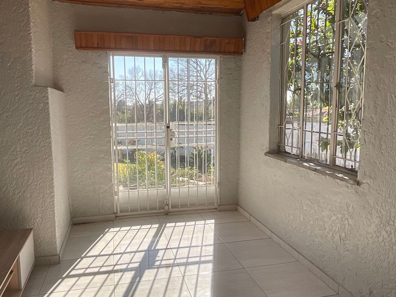An empty living area featuring tiled floors, textured walls, and a security gate leading to the garden, providing a bright and functional space.