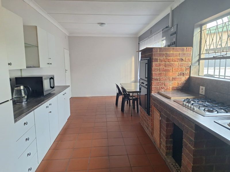 Kitchen featuring white cabinetry, a gas hob, built-in oven, and a unique brick fireplace, finished with tiled flooring and security bars on the windows.