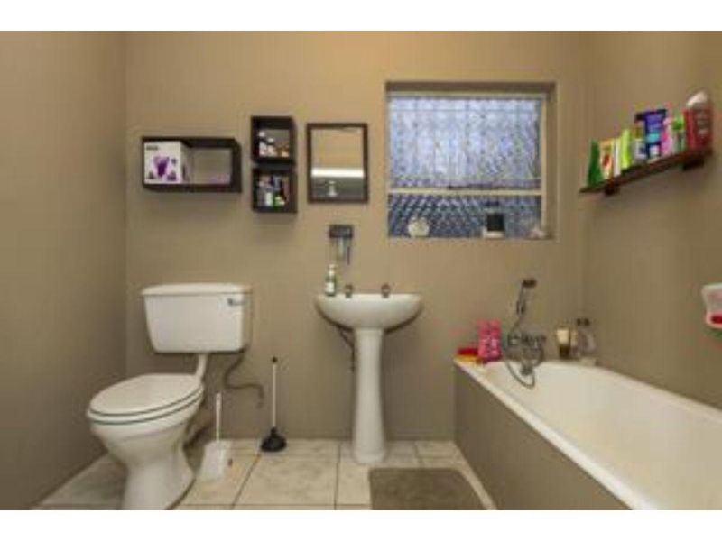 A functional bathroom featuring a pedestal basin, standard toilet, and bathtub with tiled flooring and an obscured glass window.