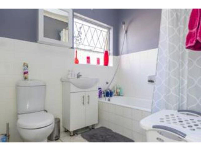 A functional bathroom featuring a white vanity basin, toilet, and a bathtub with a shower attachment, finished with tiled splashbacks.