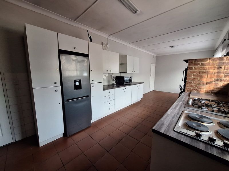 Functional kitchen featuring white cabinetry, laminate countertops, dual cooktops, and an exposed brick wall, offering a practical layout with potential for modern updates.