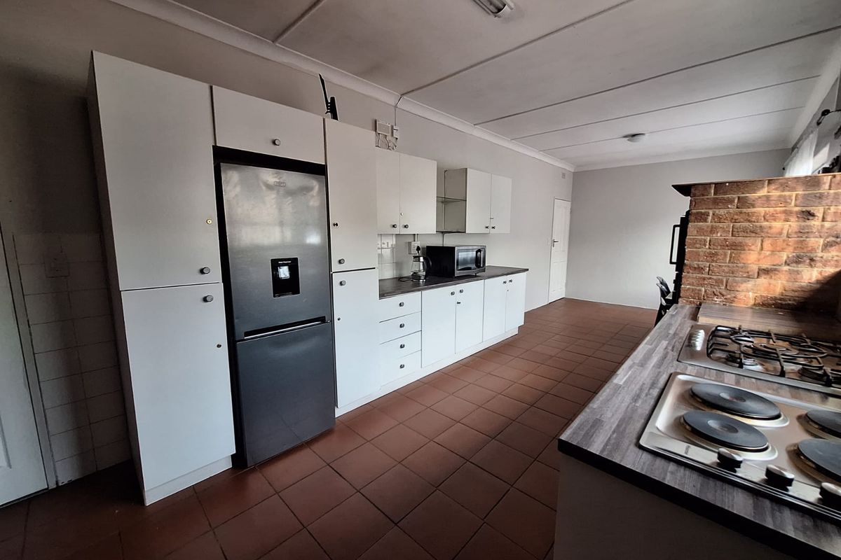 Functional kitchen featuring white cabinetry, laminate countertops, dual cooktops, and an exposed brick wall, offering a practical layout with potential for modern updates.