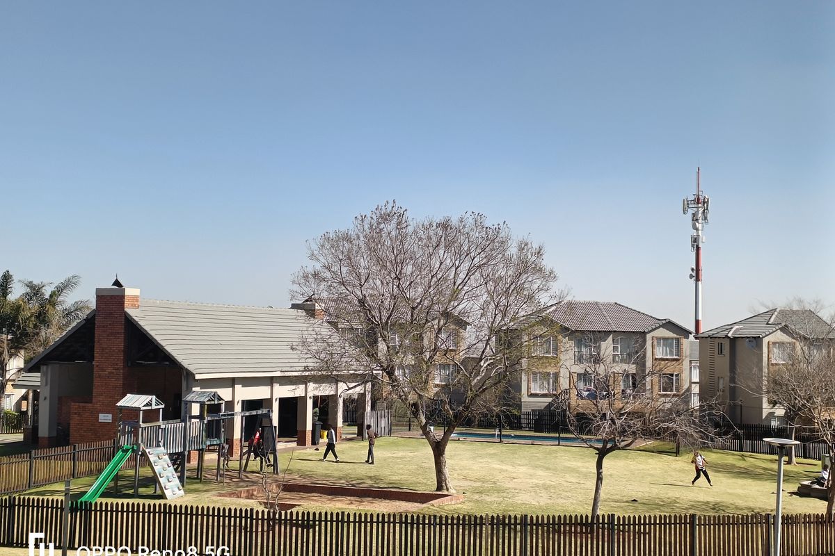 A view of a communal garden area featuring a covered patio, brick chimney, and landscaped lawn within an apartment complex.