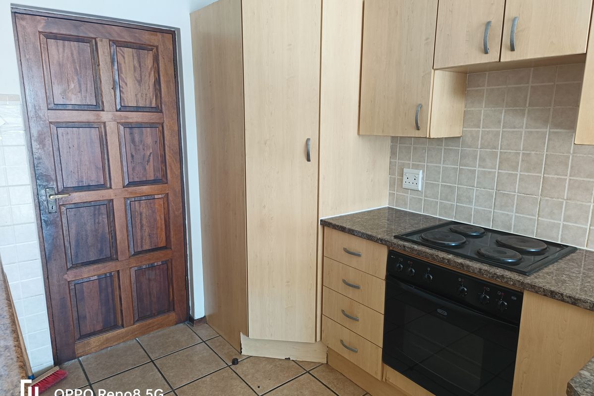 A functional kitchen area featuring light wood cabinetry, granite-look laminate countertops, a built-in oven and hob, and tiled flooring.