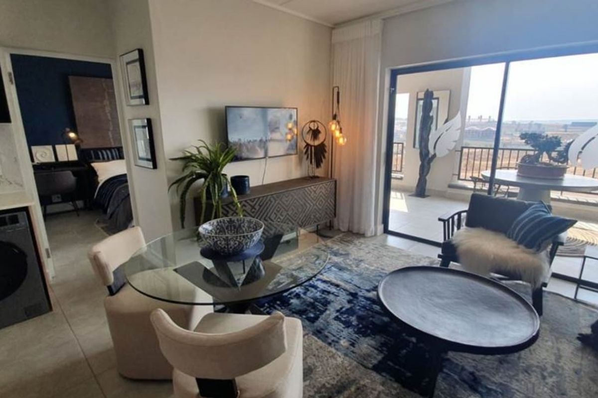 Open-plan living area featuring tiled floors, integrated laundry cabinetry, and large sliding doors leading to a private balcony with scenic views.