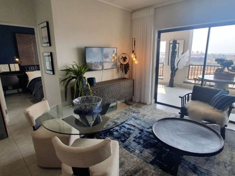 Open-plan living area featuring tiled floors, integrated laundry cabinetry, and large sliding doors leading to a private balcony with scenic views.