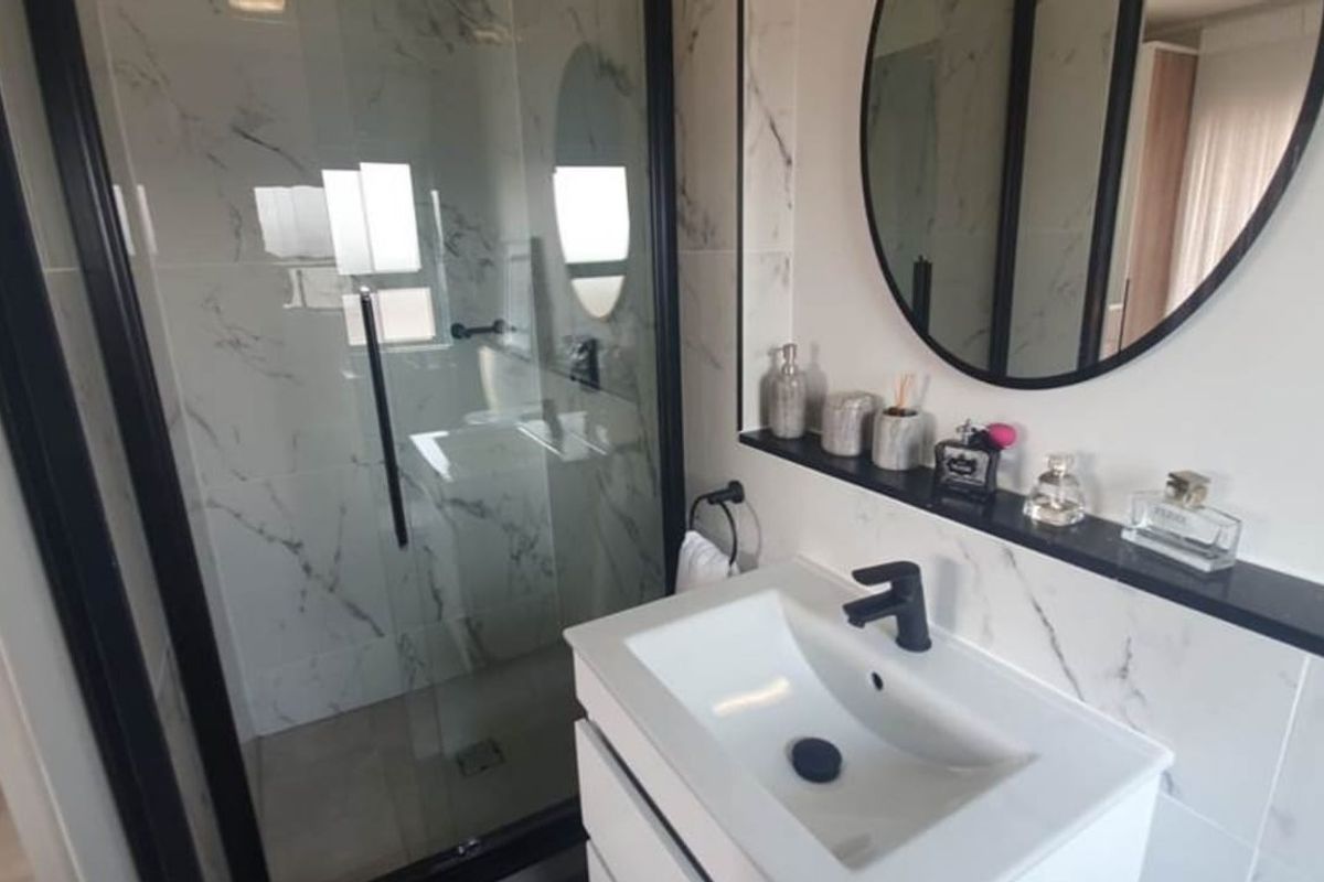 Modern bathroom featuring a walk-in shower with black frame, marble-look wall tiles, and a contemporary vanity with black tapware.