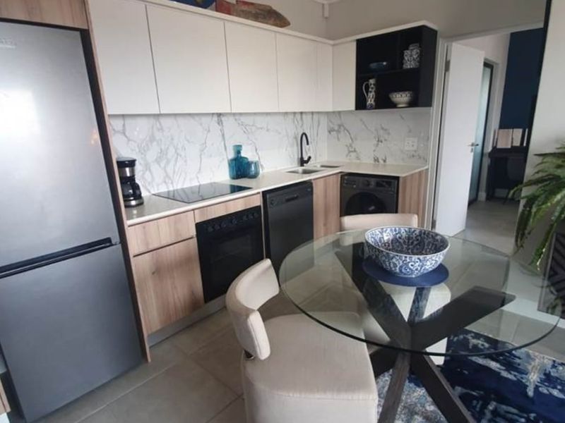 Modern open-plan kitchen featuring sleek wood-tone cabinetry, marble-look splashbacks, and integrated appliances, seamlessly flowing into the dining area.