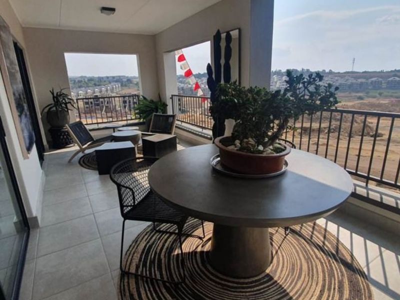 A spacious covered balcony featuring tiled flooring and a metal balustrade, offering expansive views of the surrounding area.