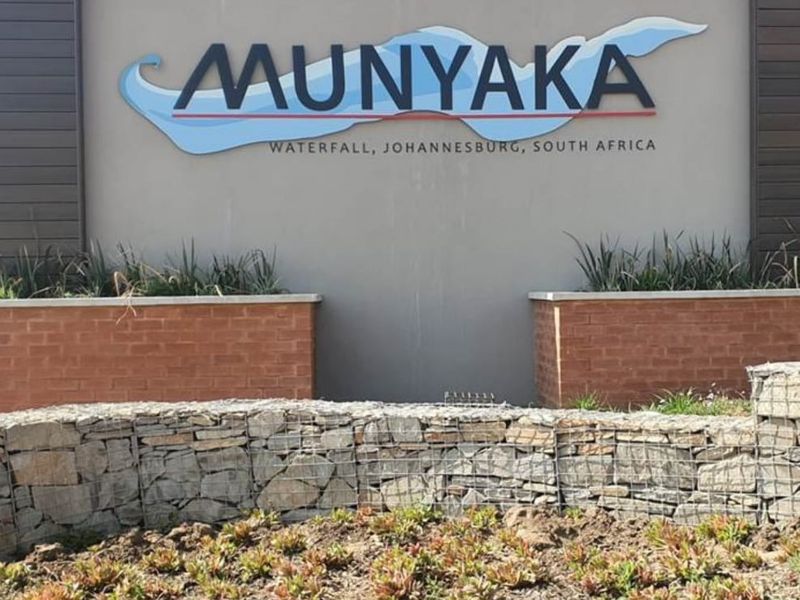 The entrance signage for Munyaka estate in Waterfall, Johannesburg, featuring modern gabion stone walling and brick planter boxes.