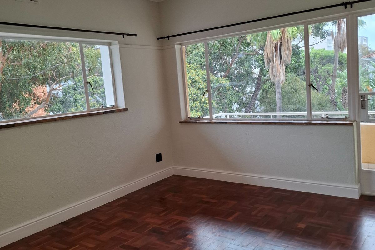 A bright, empty living room featuring polished parquet flooring, large casement windows with timber sills, and modern recessed lighting.