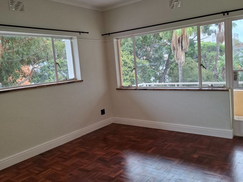 A bright, empty living room featuring polished parquet flooring, large casement windows with timber sills, and modern recessed lighting.