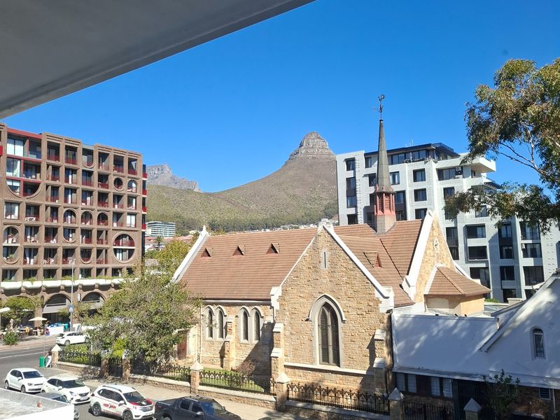 A clear, elevated view overlooking a historic stone church, surrounding urban architecture, and the iconic Lion's Head mountain peak.
