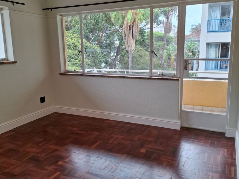 Bright and spacious living area featuring classic parquet flooring, large windows, and direct access to an outdoor balcony.