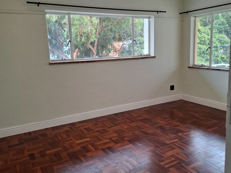 A bright, empty bedroom featuring polished parquet flooring, recessed downlights, and large windows with timber sills, offering a clean and neutral living space.