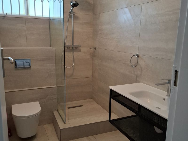 Modern bathroom featuring a walk-in shower with glass screen, wall-mounted toilet, and a contemporary vanity basin with neutral floor-to-ceiling tiling.