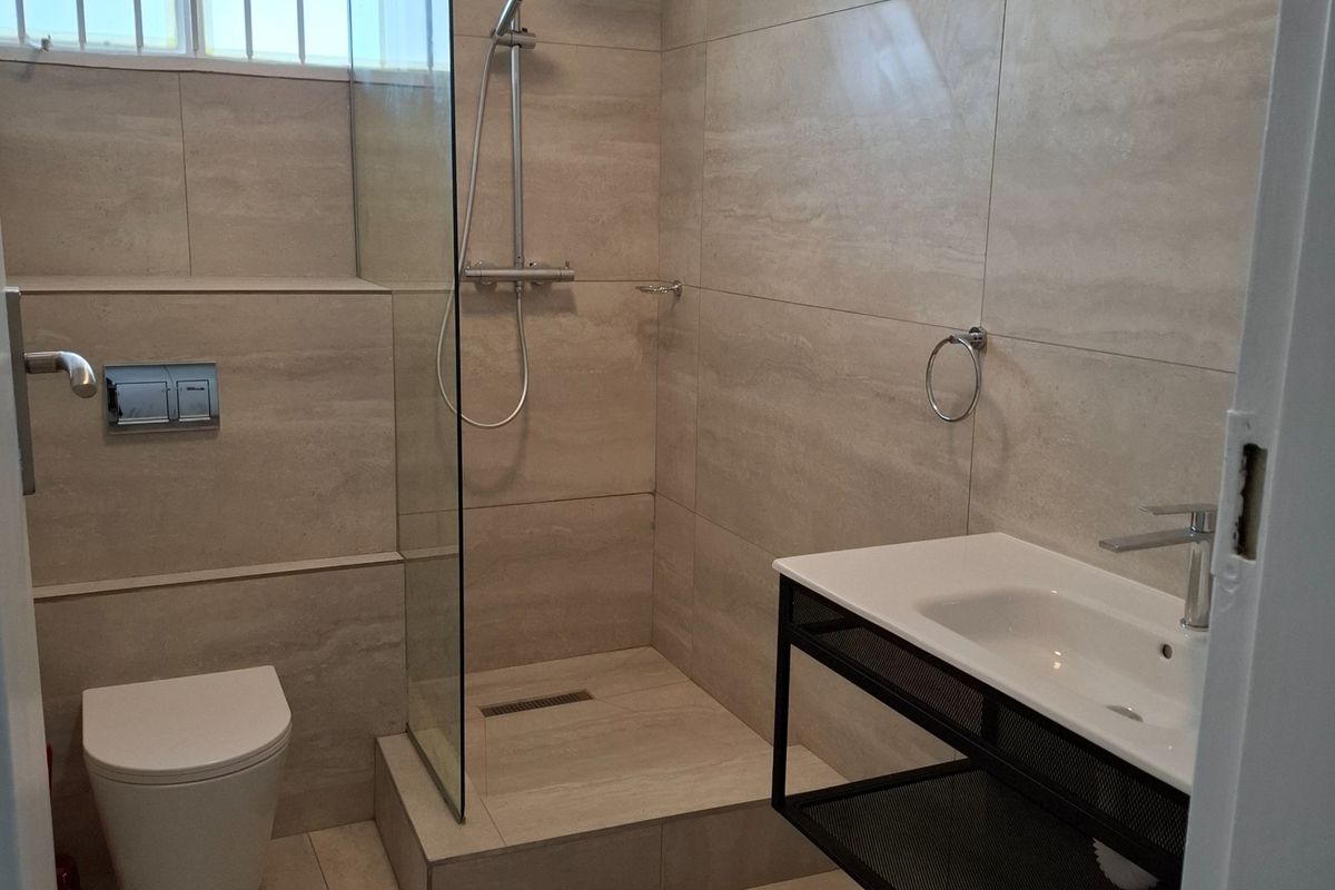 Modern bathroom featuring a walk-in shower with glass screen, wall-mounted toilet, and a contemporary vanity basin with neutral floor-to-ceiling tiling.