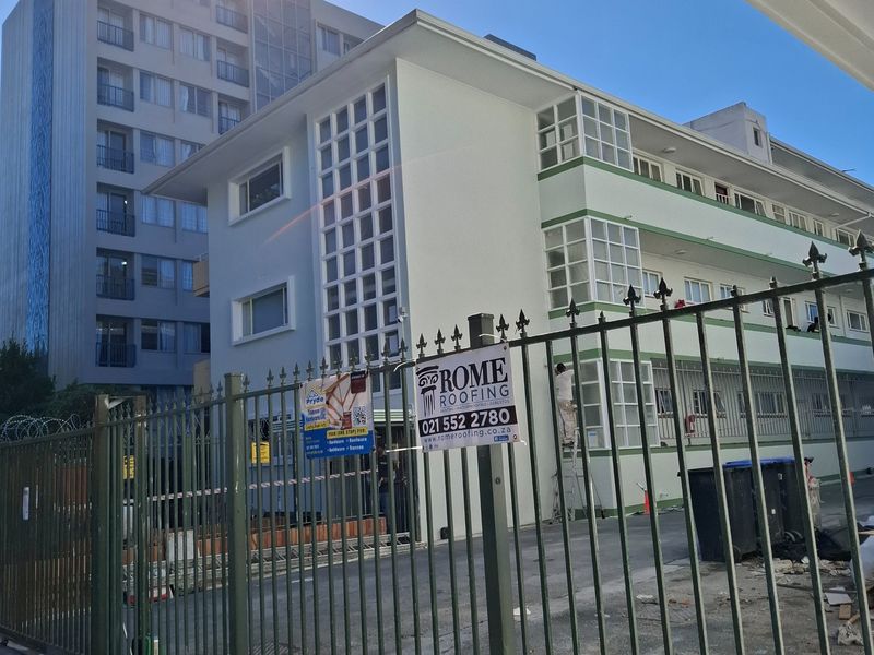 Exterior view of an apartment building complex featuring a metal security fence and paved driveway area.