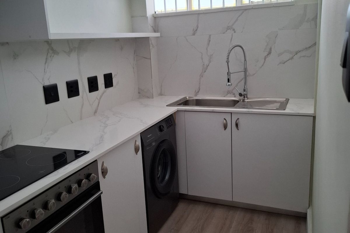 Modern, renovated kitchen featuring marble-look splashbacks, sleek white cabinetry, built-in oven with hob, and durable laminate flooring.
