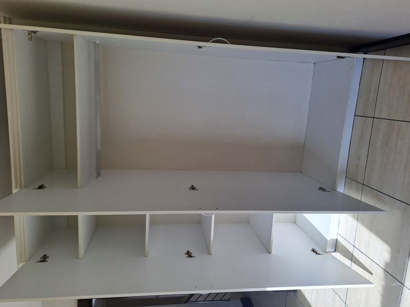 A bedroom featuring a white built-in wardrobe with shelving and hanging space, complemented by neutral tiled flooring.