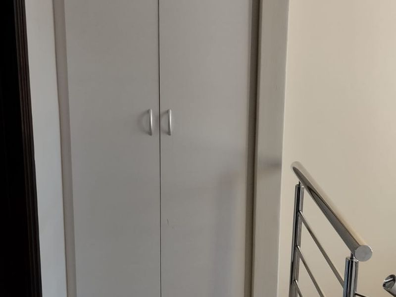 A functional hallway area featuring a built-in storage cupboard and a modern stainless steel balustrade overlooking the staircase.