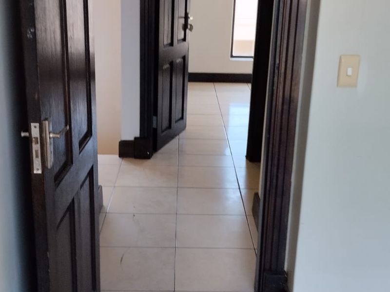A view through a series of doorways into a tiled hallway, featuring dark timber door frames and skirting boards.