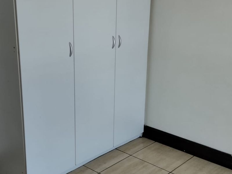 A simple bedroom featuring neutral tiled flooring and a white built-in wardrobe with modern handles.