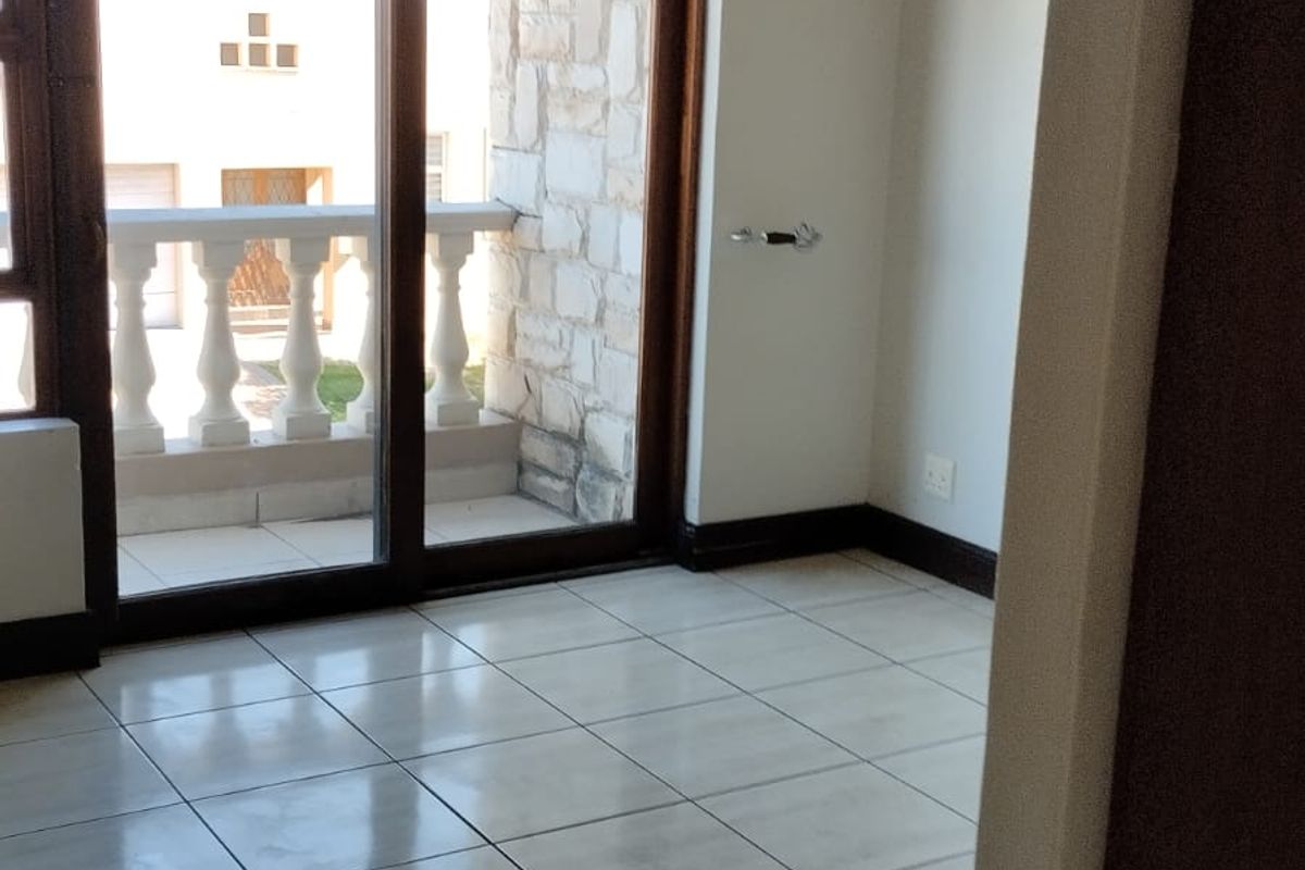 An empty bedroom featuring tiled flooring, neutral walls, and a sliding glass door providing direct access to a private balcony.